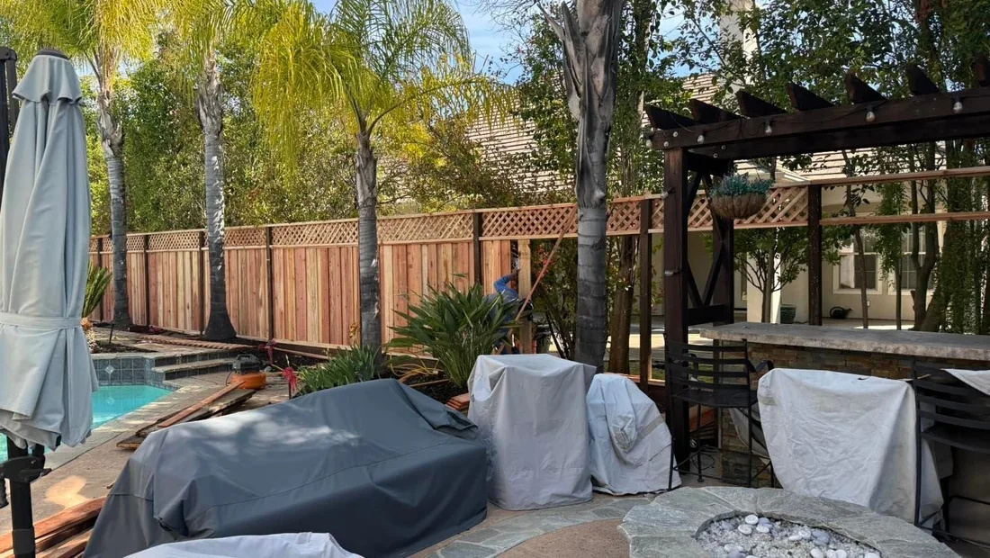 Backyard fence line running behind a pergola and covered patio furniture